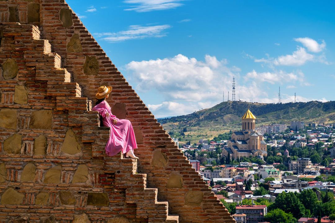 Woman in a vibrant dress ascending the steps of Narikala Fortress, overlooking Tbilisi, Georgia